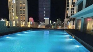 Une piscine la nuit, avec les bâtiments de la ville en arrière-plan.
