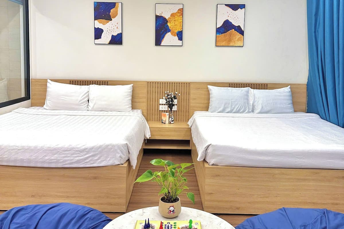A hotel room with two beds, a small table with a board game, and three abstract paintings on the wall.
