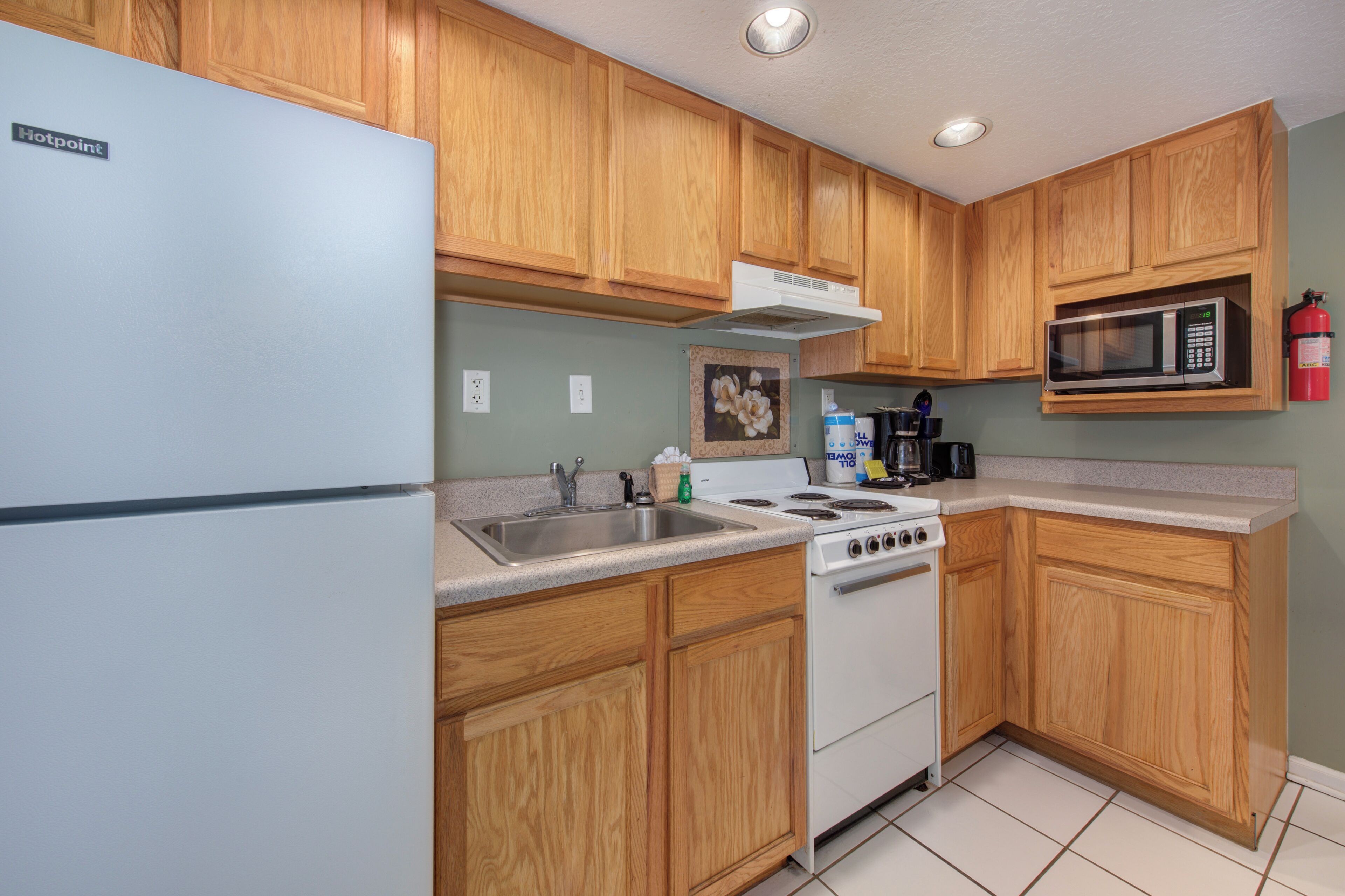 A kitchen with wooden cabinets, a white refrigerator, a stove, a microwave, and a sink.