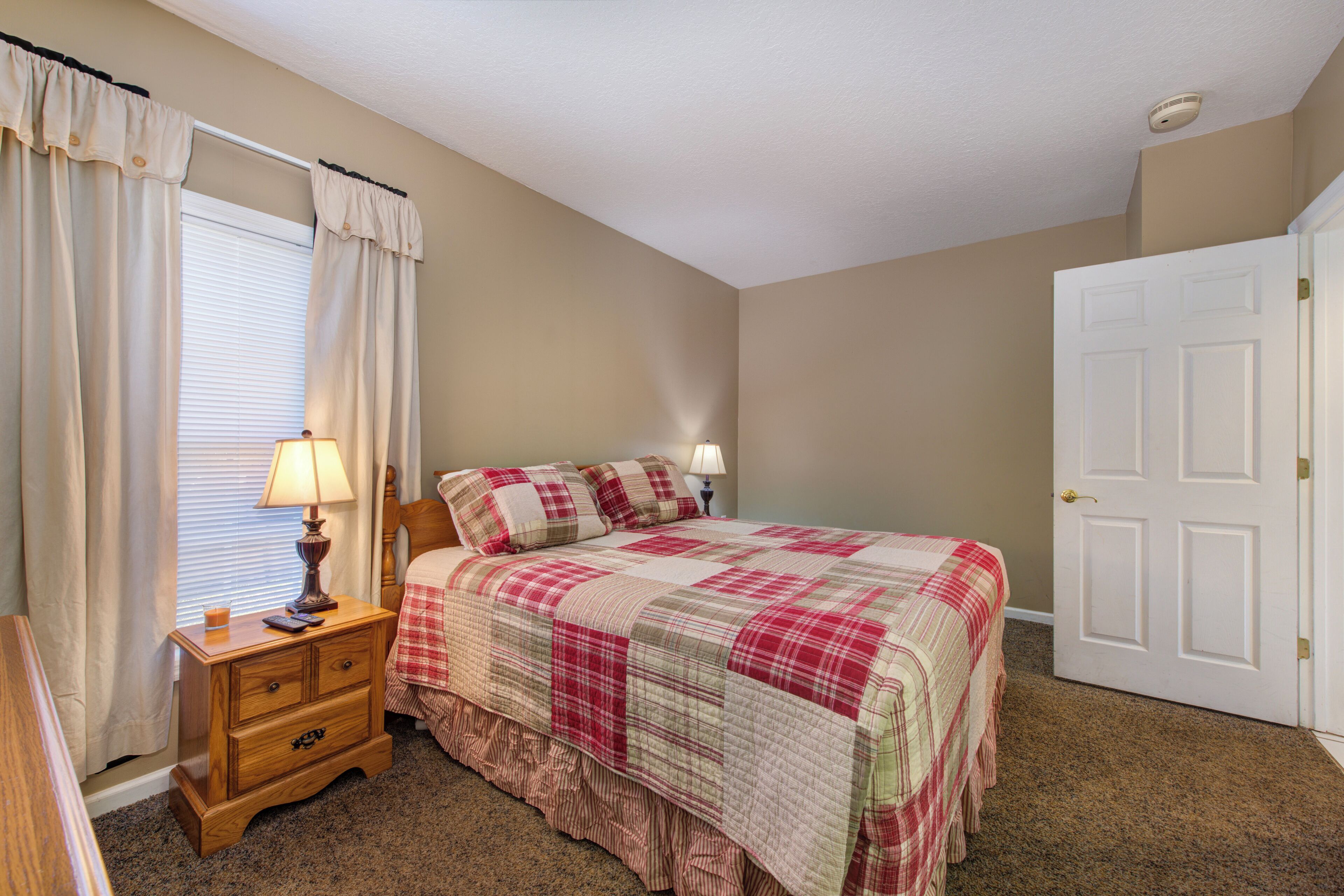 A bedroom with a bed, nightstand, lamp, and a door.