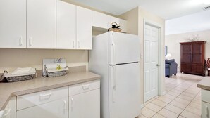 A kitchen with white cabinets, a refrigerator, and a countertop with baskets and a tray. - Vanderbilt Villas (Naples)
