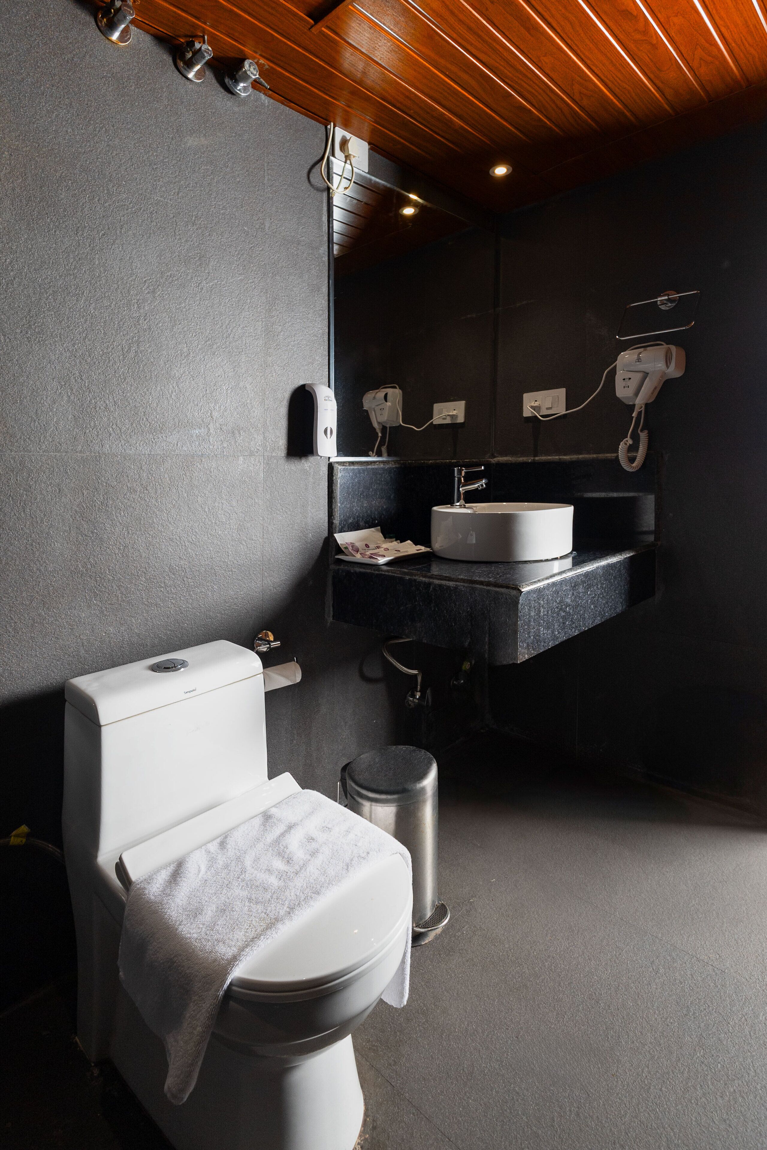 Une salle de bain moderne avec des toilettes blanches, un lavabo doté d’un plan-vasque noir et un miroir au-dessus du lavabo.