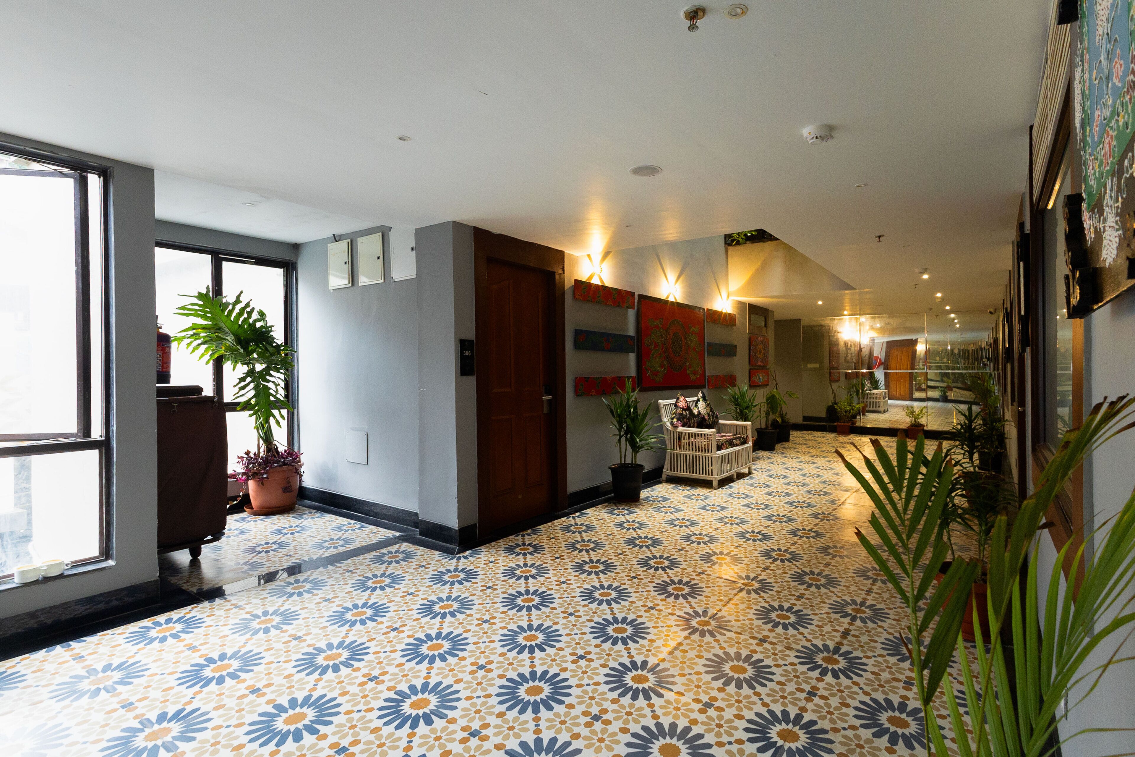 A hallway with patterned floor tiles, potted plants, and a wooden door.