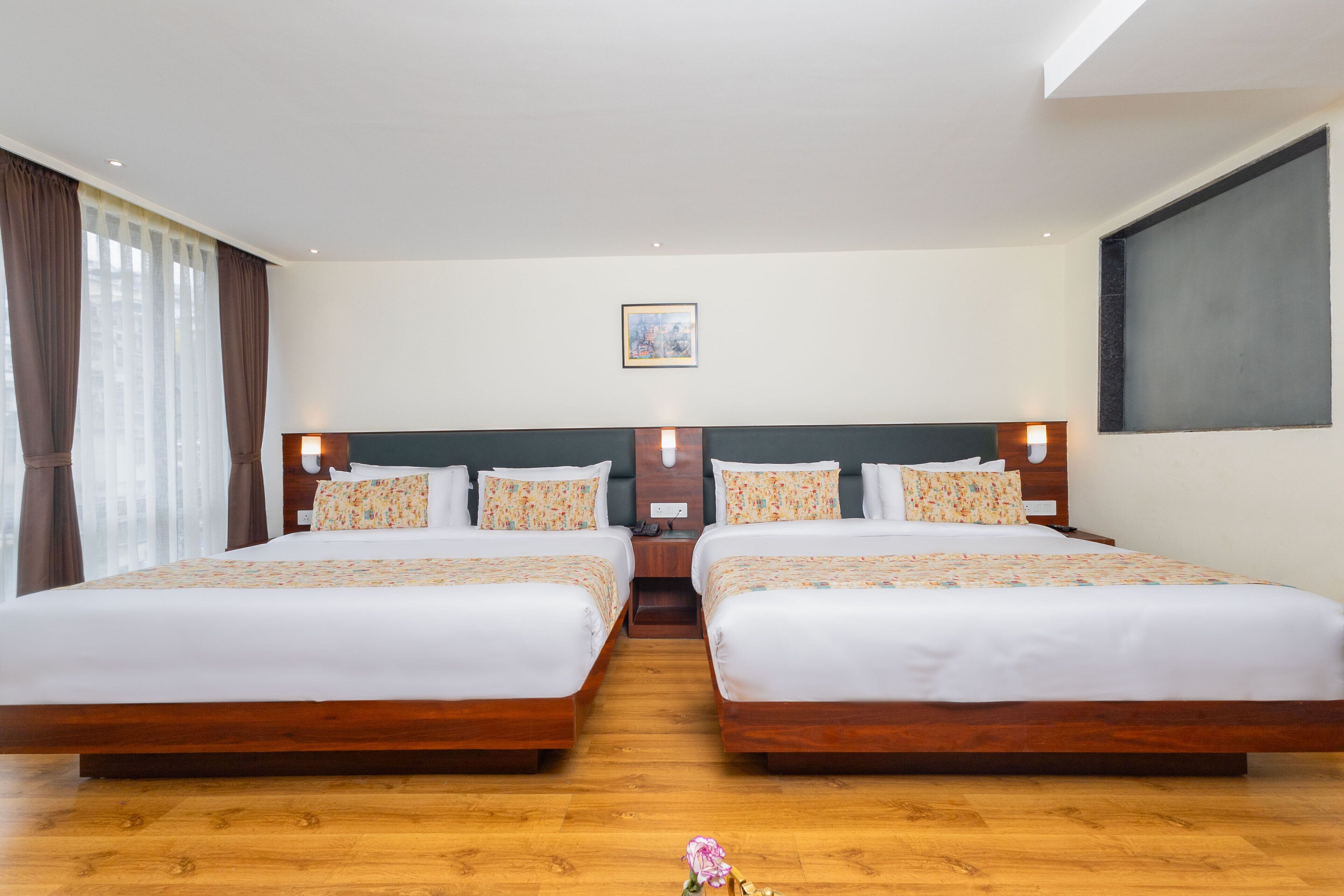 Habitación doble con dos camas, cabeceros de madera y un ventanal grande con cortinas.