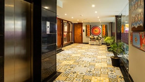 A hotel lobby with a tiled floor, an elevator, a reception desk, and a wall with colorful artwork. - Sumitel JB Park Darjeeling  (Darjeeling)