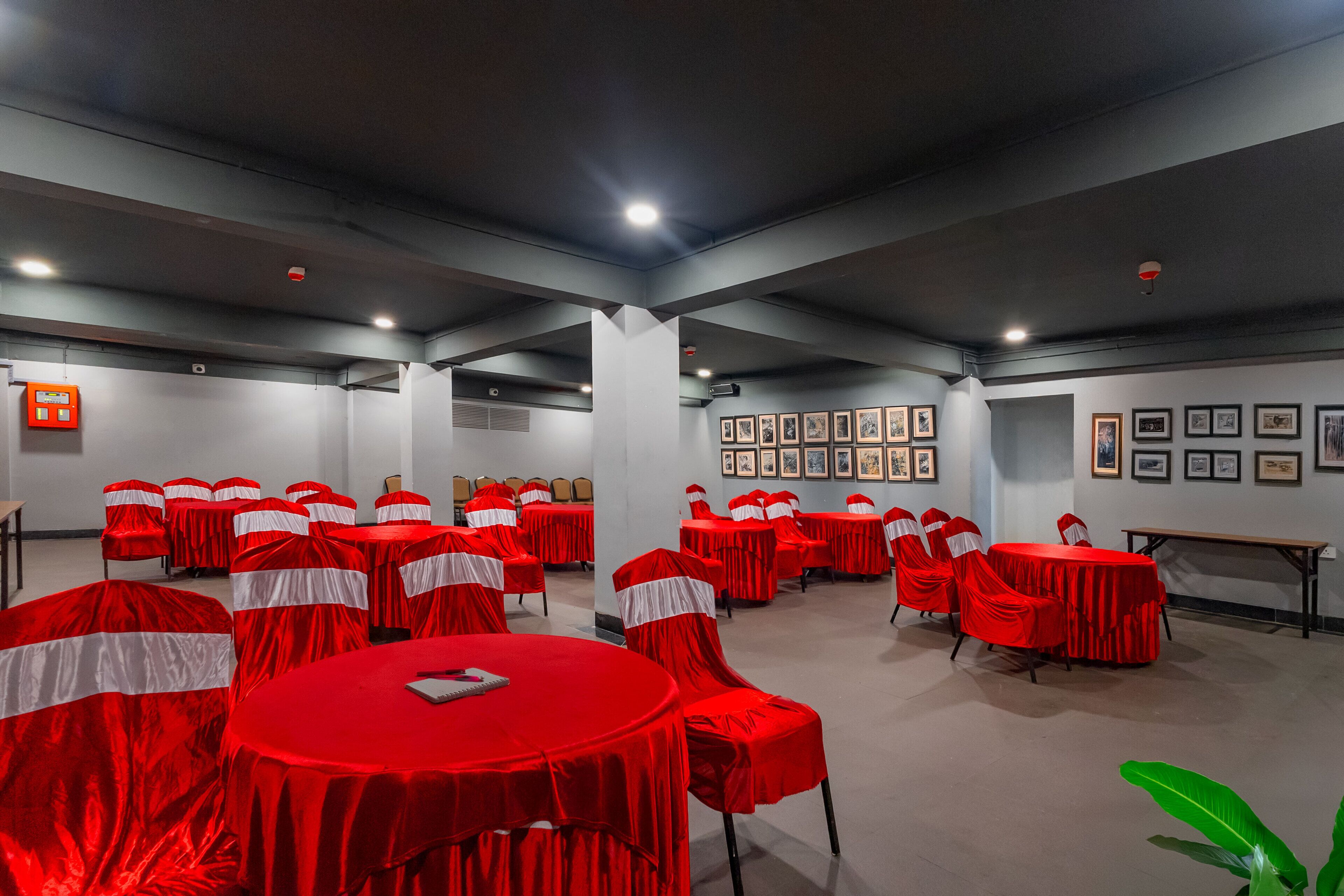 Uma sala de conferências com várias mesas e cadeiras, toalhas vermelhas e quadros nas paredes.