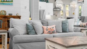 Una sala de estar moderna con un sofá gris, una mesa de centro de madera y una cocina con gabinetes blancos y un letrero que dice "Beach".