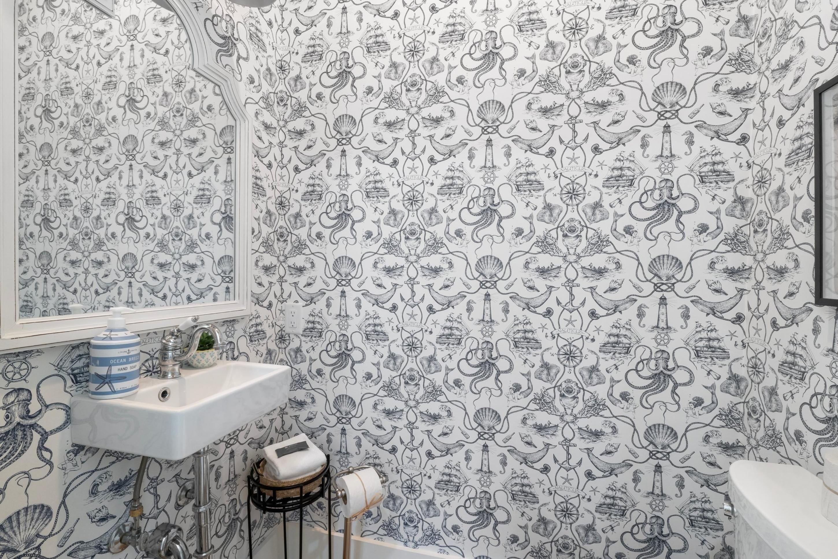 Un baño con papel tapiz de temática náutica, un lavabo blanco y un espejo.