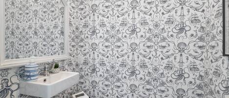 Un baño con papel tapiz de temática náutica, un lavabo blanco y un espejo.