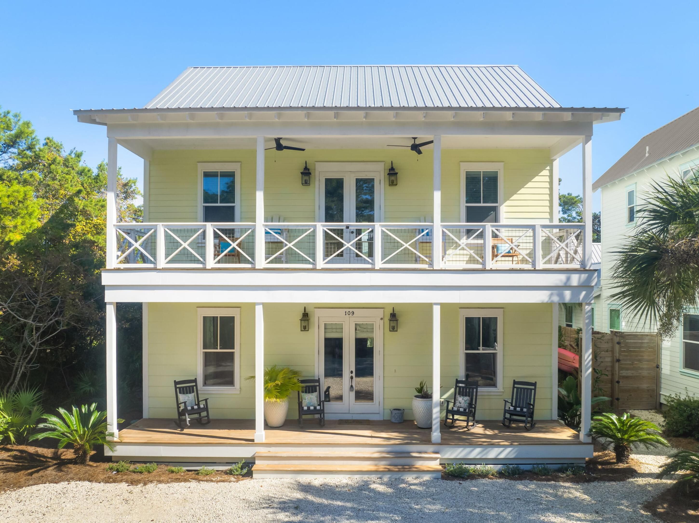 A two-story house with a balcony, a porch with chairs, and a front door.