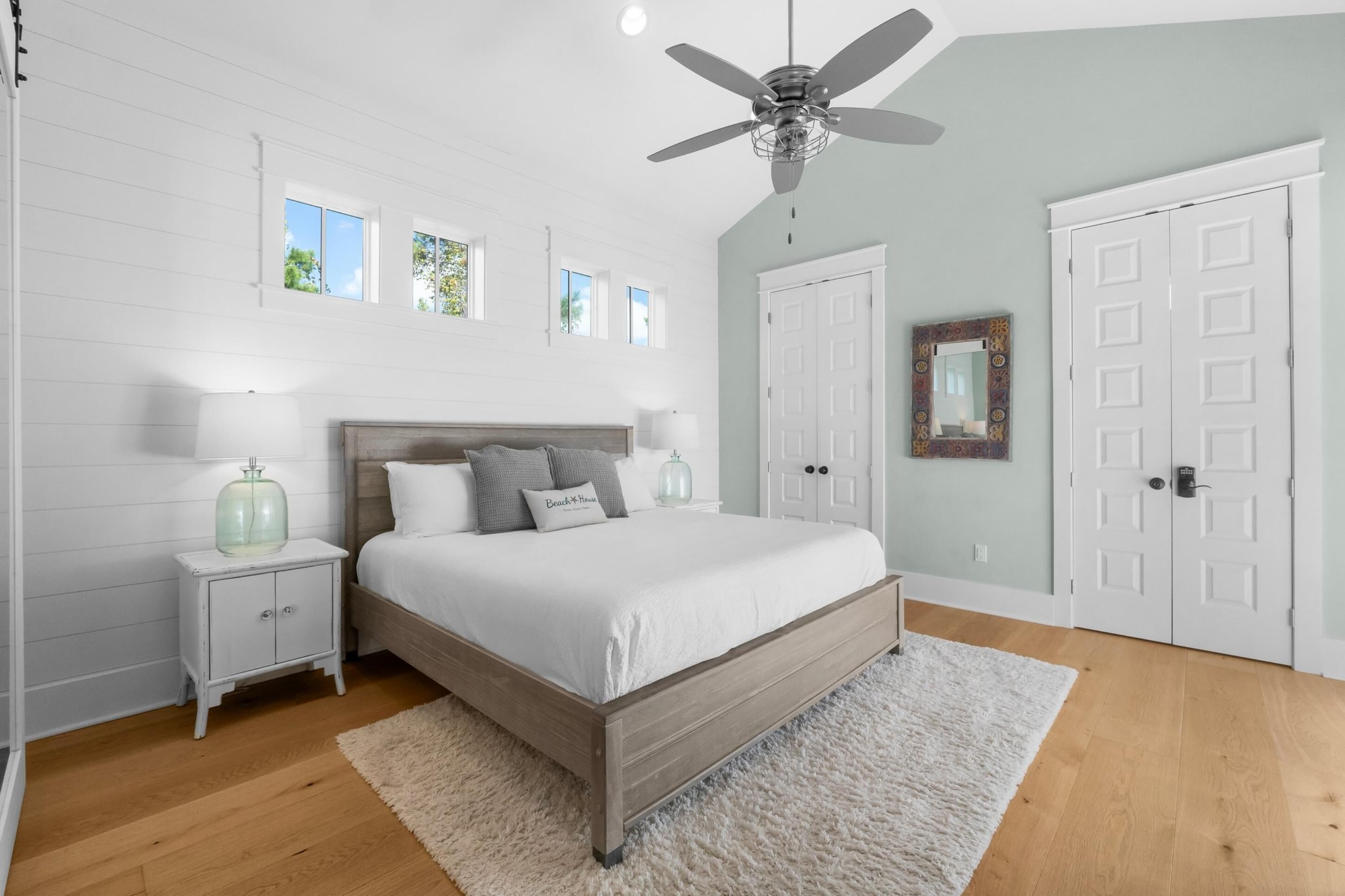 A bedroom with a wooden bed, white nightstands, a ceiling fan, and a large mirror.