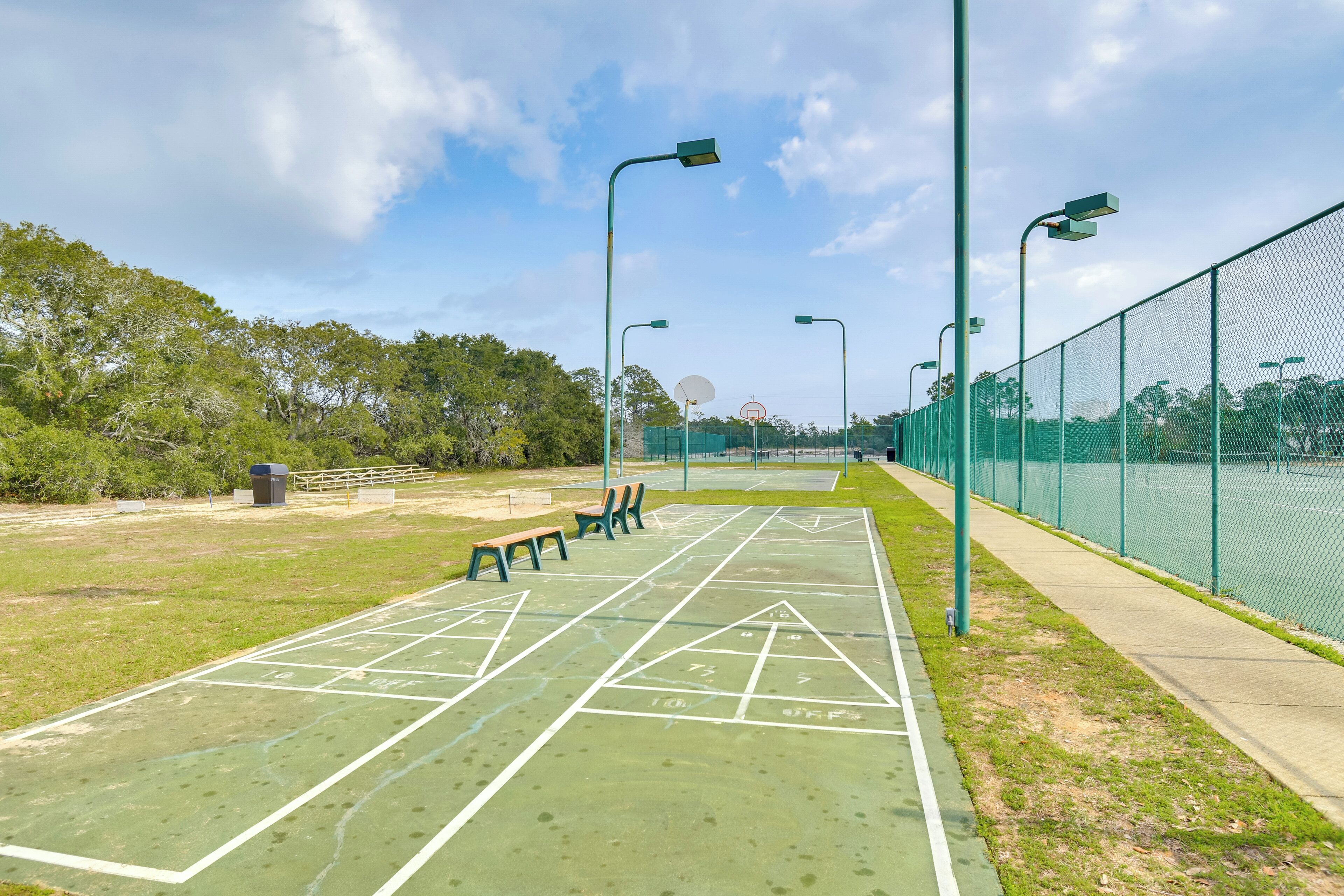 A green outdoor shuffleboard court with benches and street lamps.