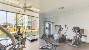 Ein Fitnessstudio mit unterschiedlichen Trainingsgeräten, großen Fenstern und einem Deckenventilator.