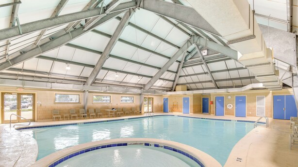 Ein Innenpool mit hoher Decke und Dachfenstern, umgeben von Liegestühlen und Umkleideräumen.