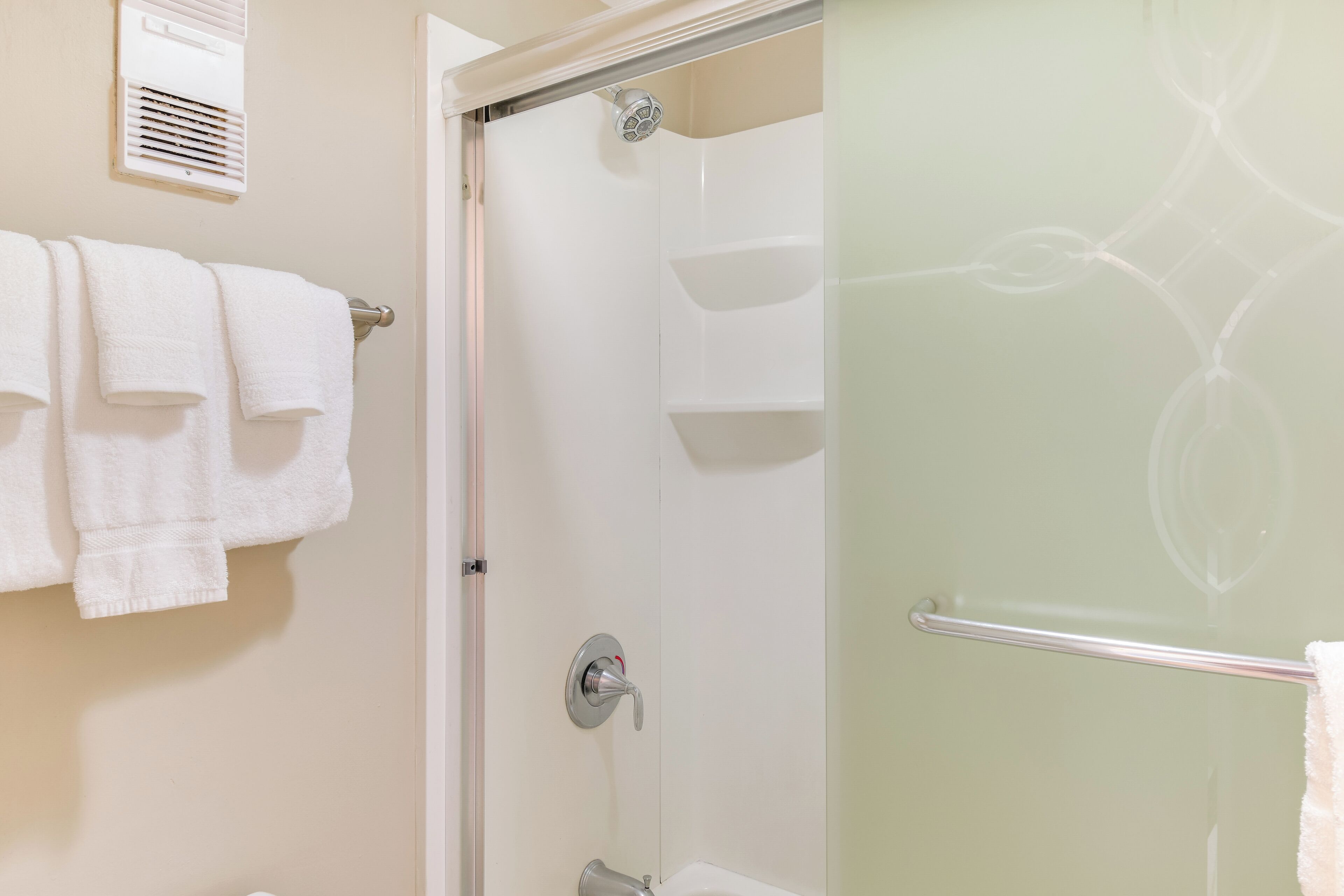 A bathroom with a glass shower enclosure, a towel rack with towels, and a wall-mounted heater.