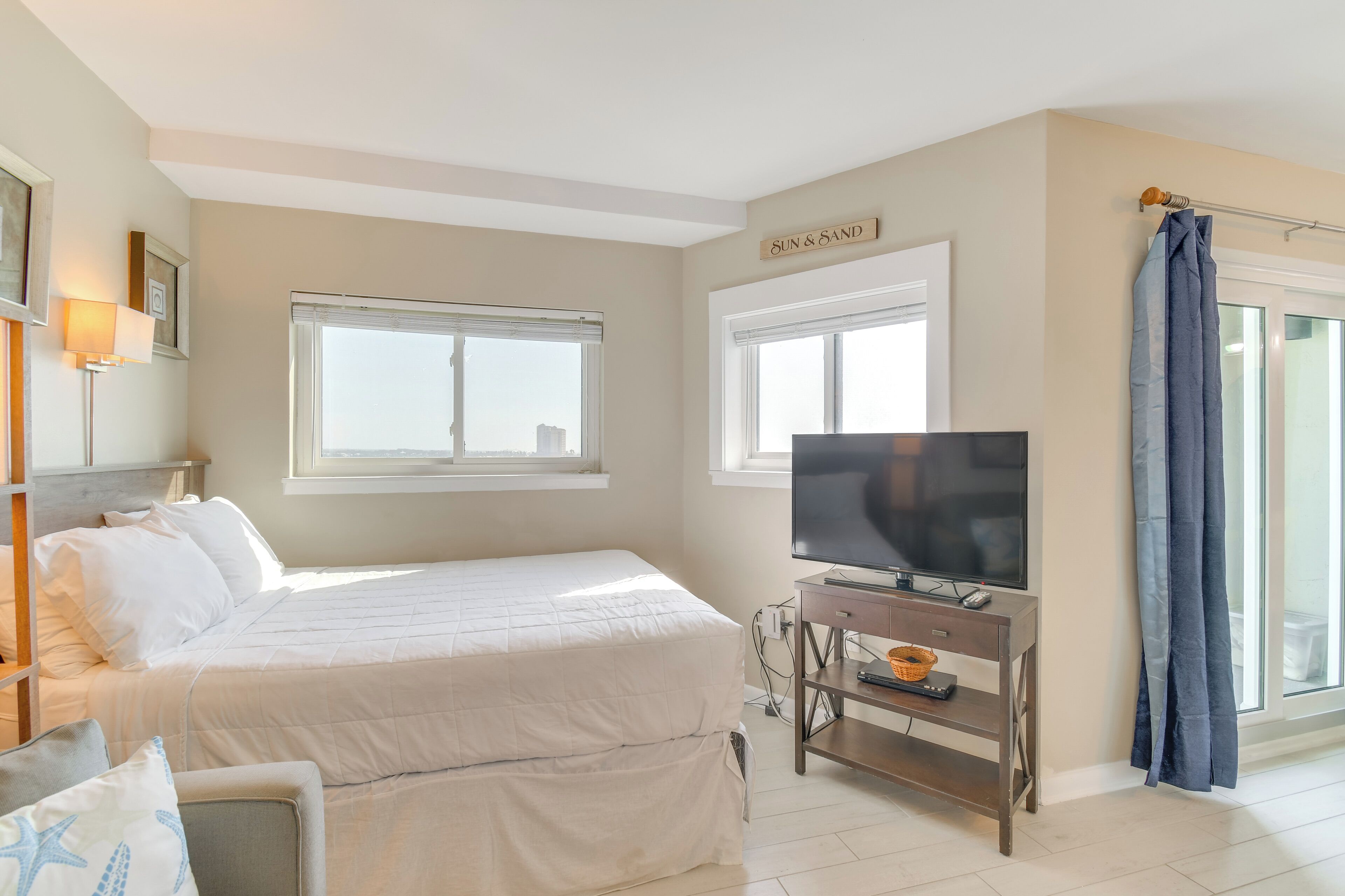 Un dormitorio con una cama, un televisor sobre un mueble, una ventana y un cartel que dice "SUN & SAND".