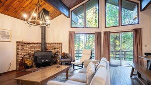 Un salon chaleureux avec une cheminée, une table en bois, un canapé et une grande fenêtre avec des rideaux.