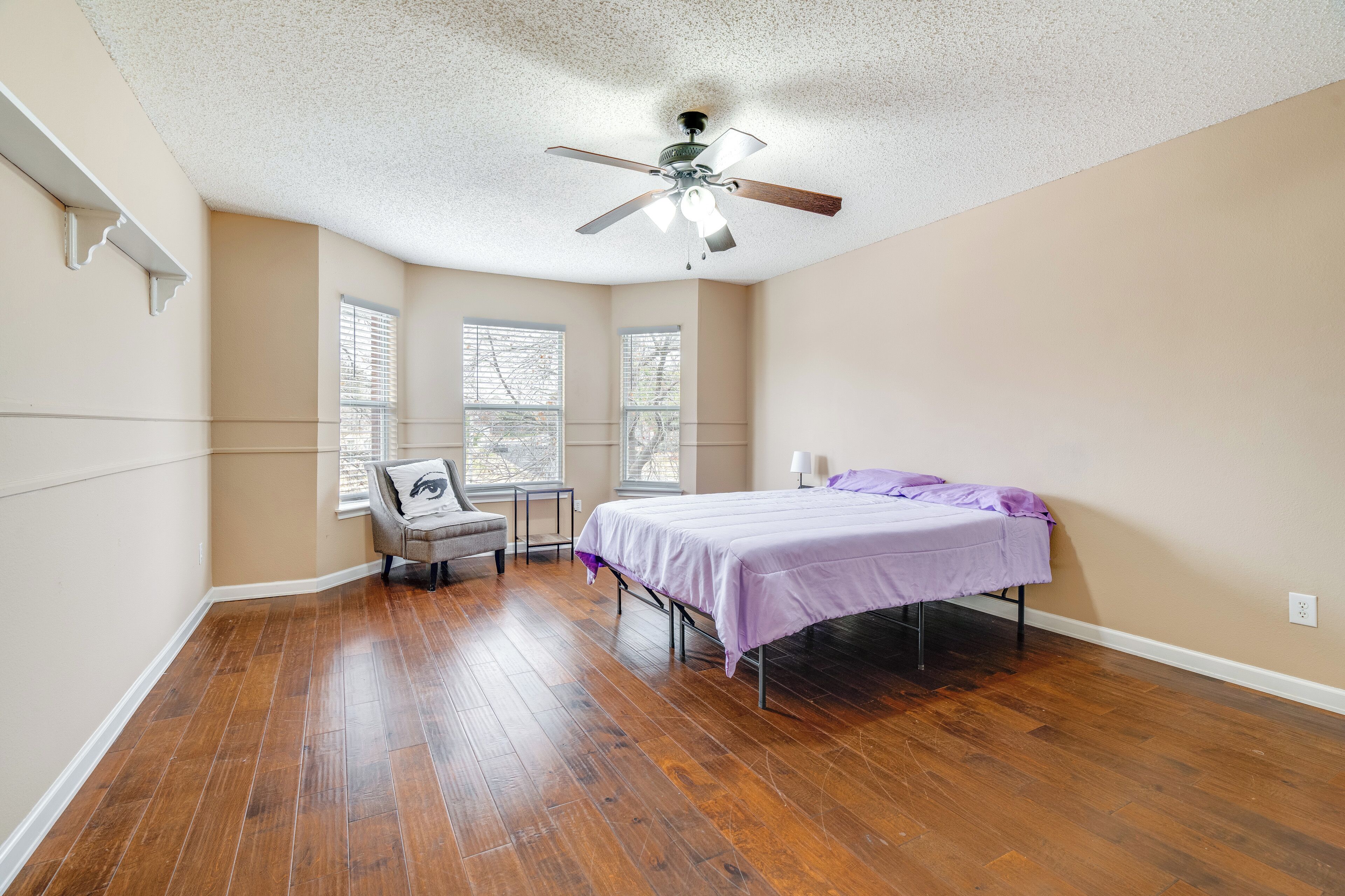 A bedroom with a bed, a chair, a desk, and a ceiling fan.
