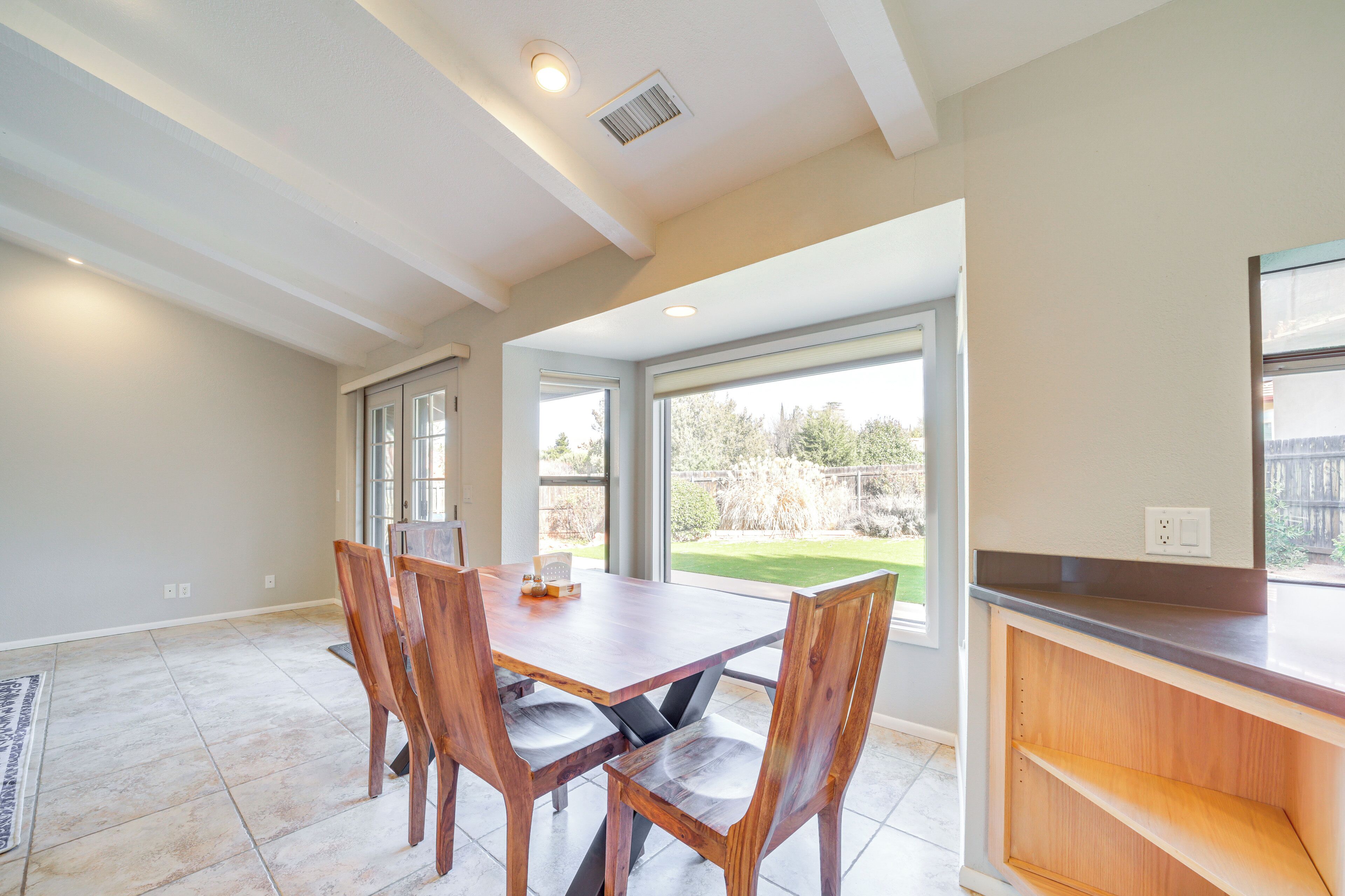 A dining area with a wooden table and chairs, large windows, and a view of a backyard.
