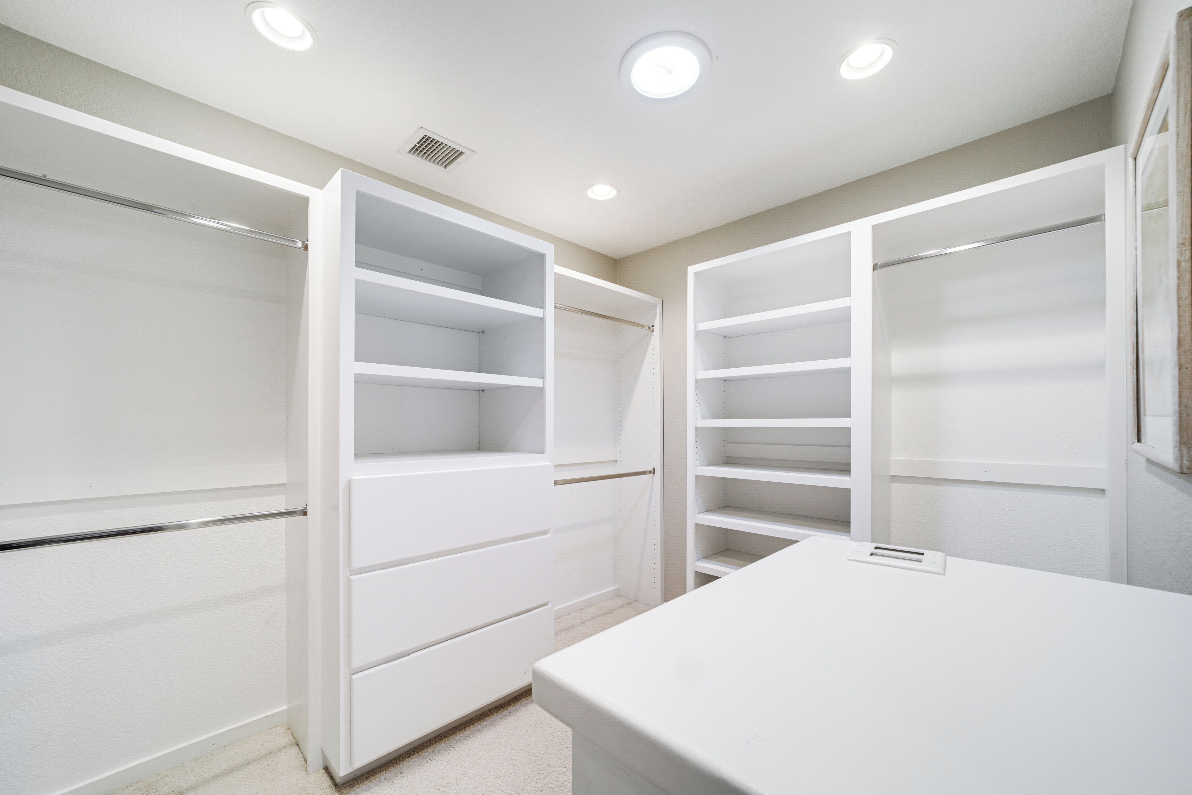 A walk-in closet with open doors, revealing multiple shelves and drawers.
