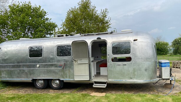 A silver recreational vehicle with a sliding door, a small kitchen area, and a sleeping berth.