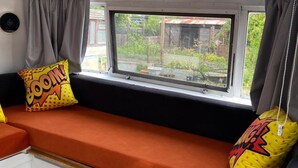 A window seat with orange cushions and two yellow pillows with comic-style text.
