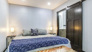 A bedroom with a bed, two bedside tables, a nightstand, a wooden bench, and a dark sliding door. - Boat Dock: Riverfront Oconto Home! (Oconto)