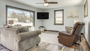 A living room with a sofa, recliner, TV, and artwork on the wall. - Boat Dock: Riverfront Oconto Home! (Oconto)