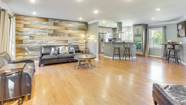 A modern living room with a stone wall, leather sofa, and a dining area with stools. - 4 Mi to Dtwn Tuscaloosa: Home w/ Cozy Den! (Tuscaloosa)