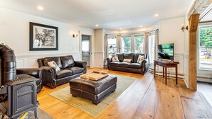 A living room with two leather sofas, a wooden coffee table, a fireplace, and a television on a wooden stand. - Walkable North Woodstock Home on Main Street! (North Woodstock)