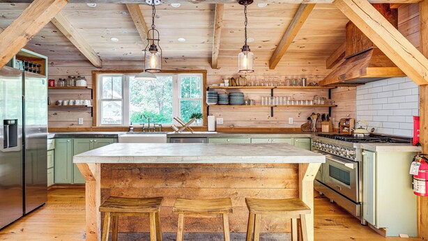 A rustic kitchen with wooden beams, a large island with stools, stainless steel appliances, and a view of greenery outside. - Walkable North Woodstock Home on Main Street! (North Woodstock)