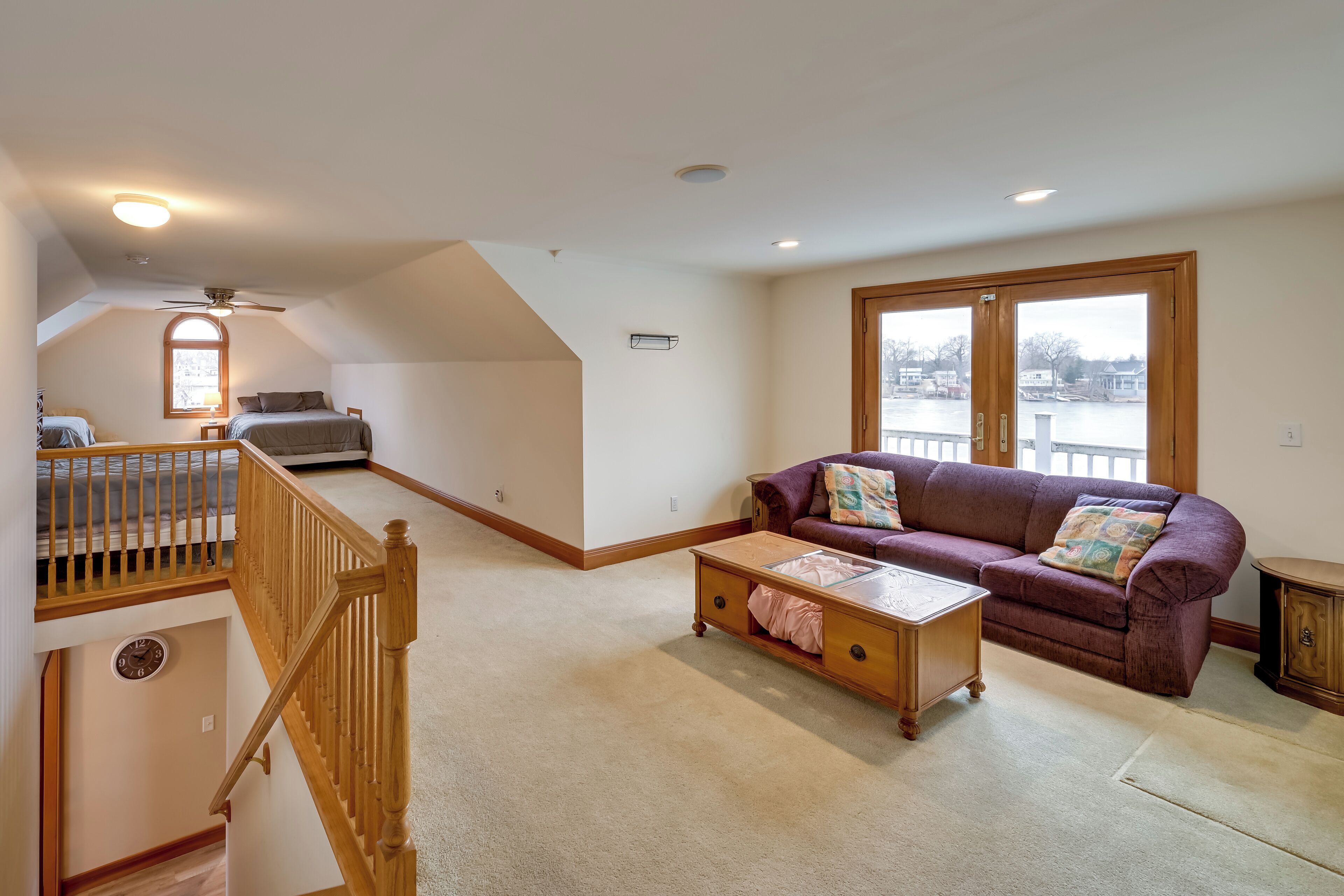 Un salón espacioso con techo alto, una escalera de madera, un sofá púrpura y un ventanal con vistas al exterior.