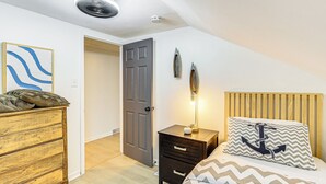 Een slaapkamer met een bed, een dressoir, een nachtkastje, een deur en een plafondventilator.