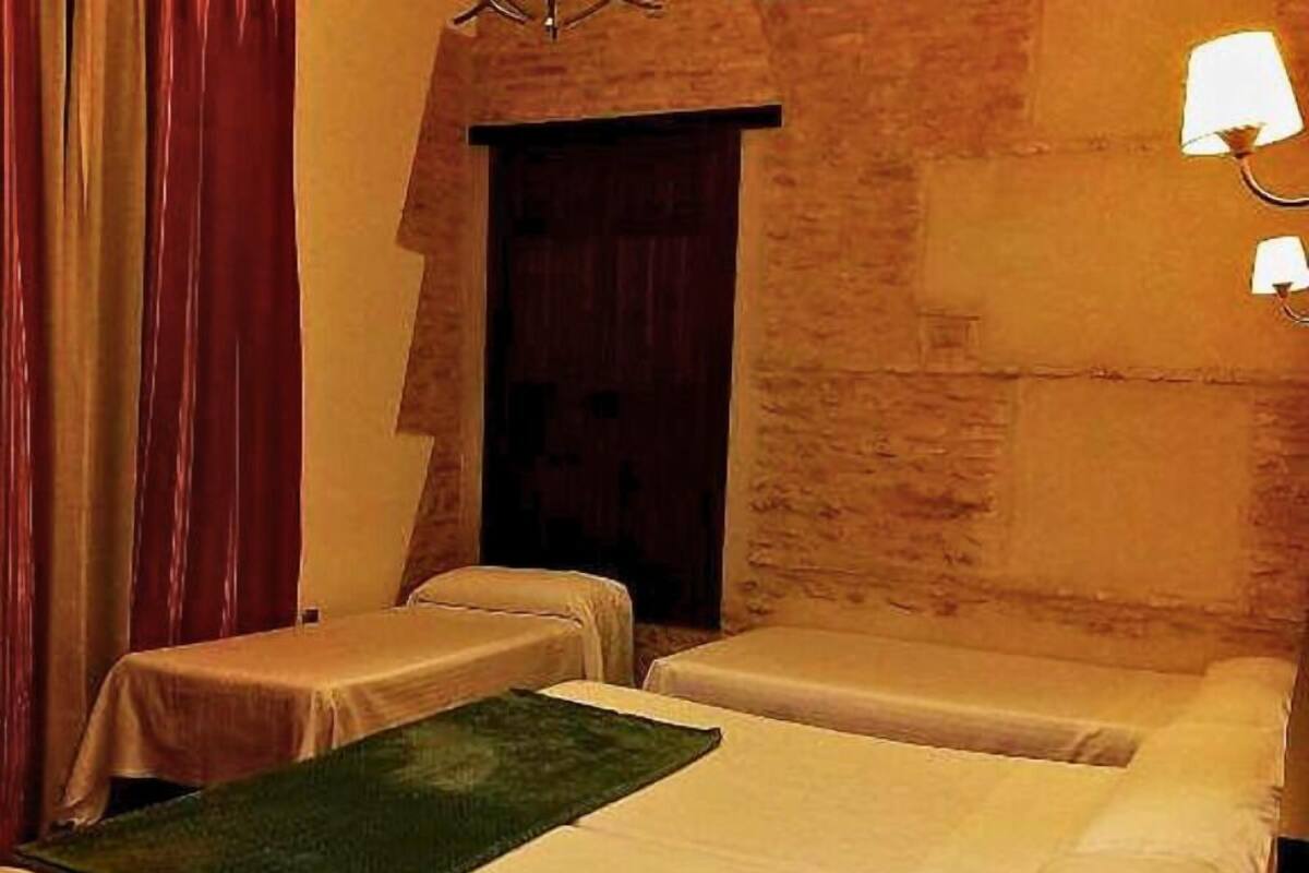 Une chambre avec deux lits, une petite table, une lampe et une porte.