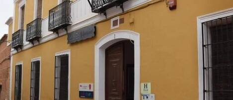 Un edificio amarillo con puerta marrón, balcones negros y banderas, incluyendo la bandera de la UE.