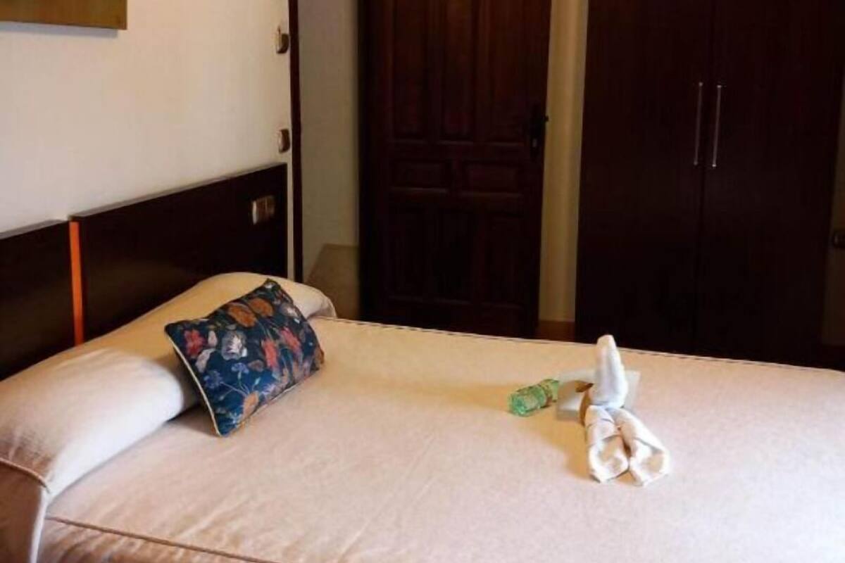 Une chambre d’hôtel avec un lit, un oreiller, une serviette pliée, une table de chevet et une armoire en bois.