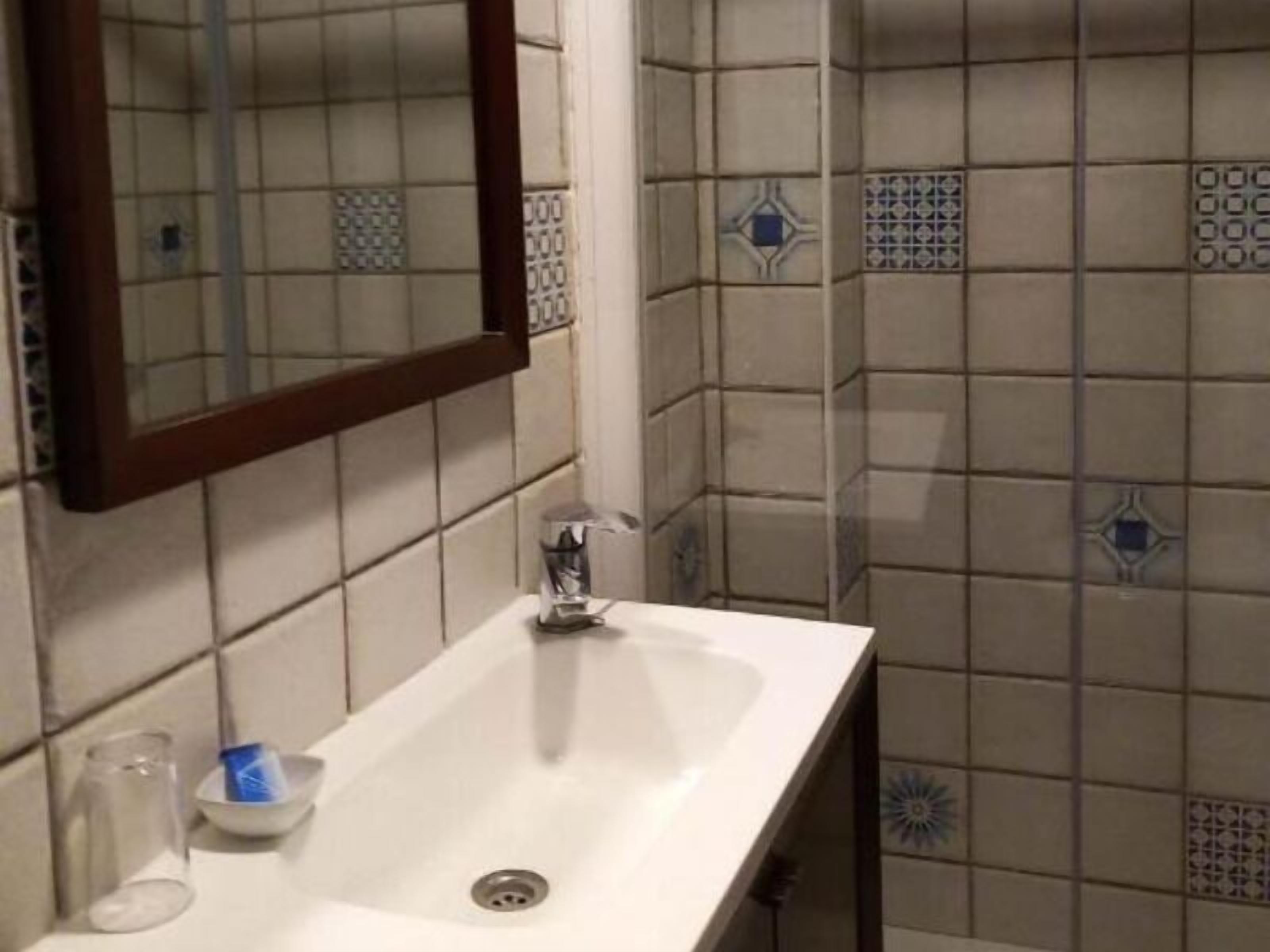 Een badkamer met een witte wastafel, een spiegel en betegelde muren.