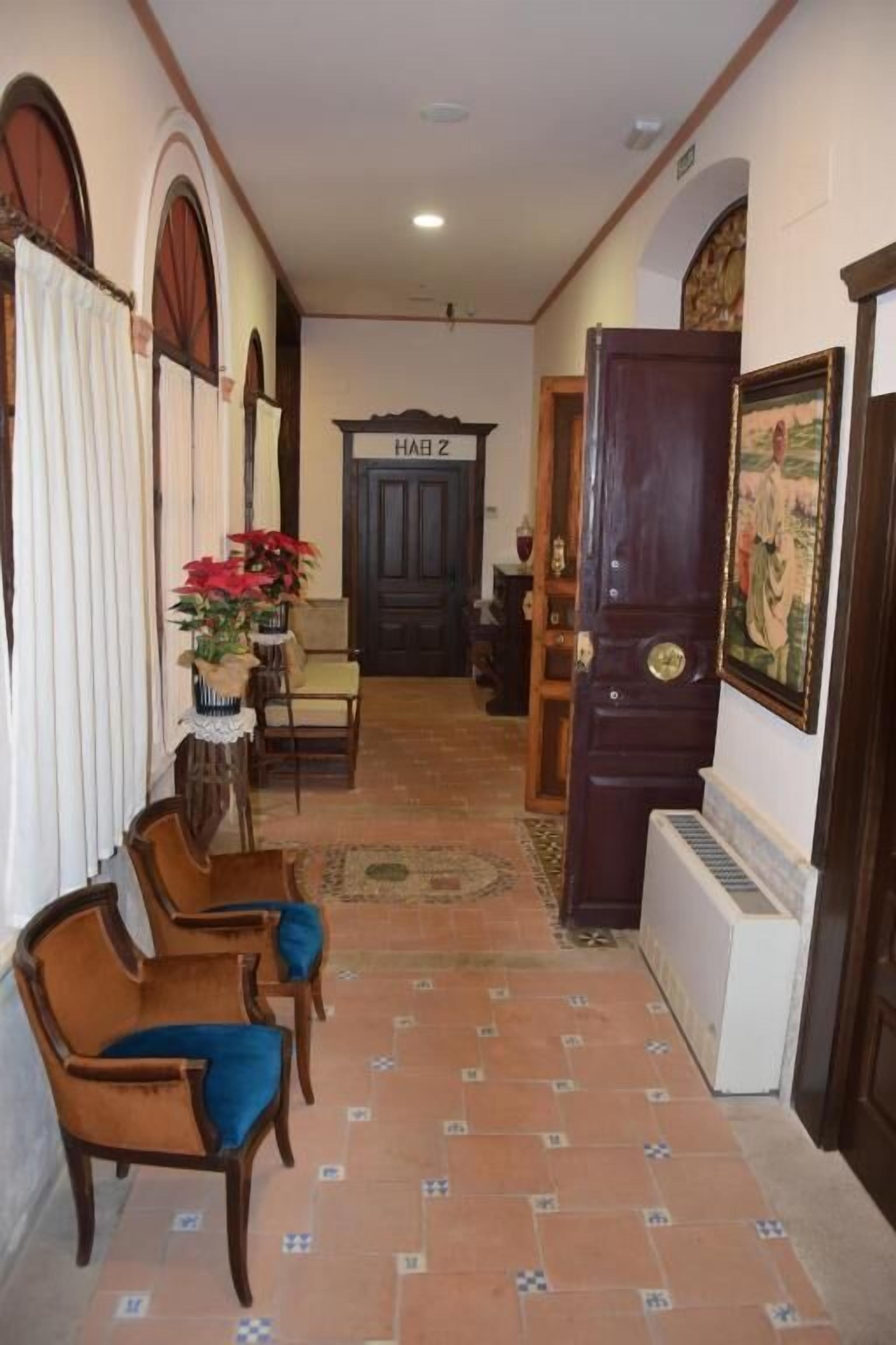 Un pasillo con suelo de baldosas, sillas de madera, una planta en maceta y una puerta con la etiqueta 'HALL 2'.