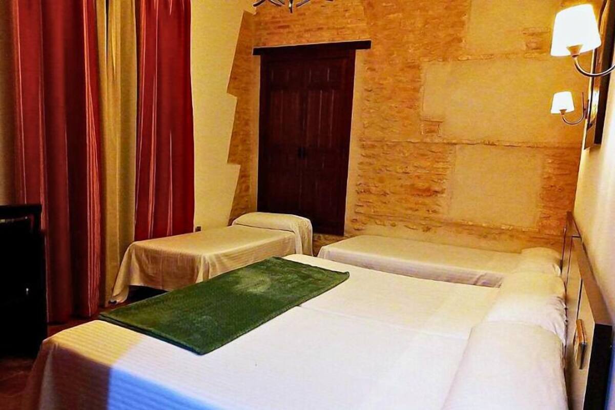 Une petite chambre d’hôtel avec deux lits simples, une porte en bois et un mur en pierre.