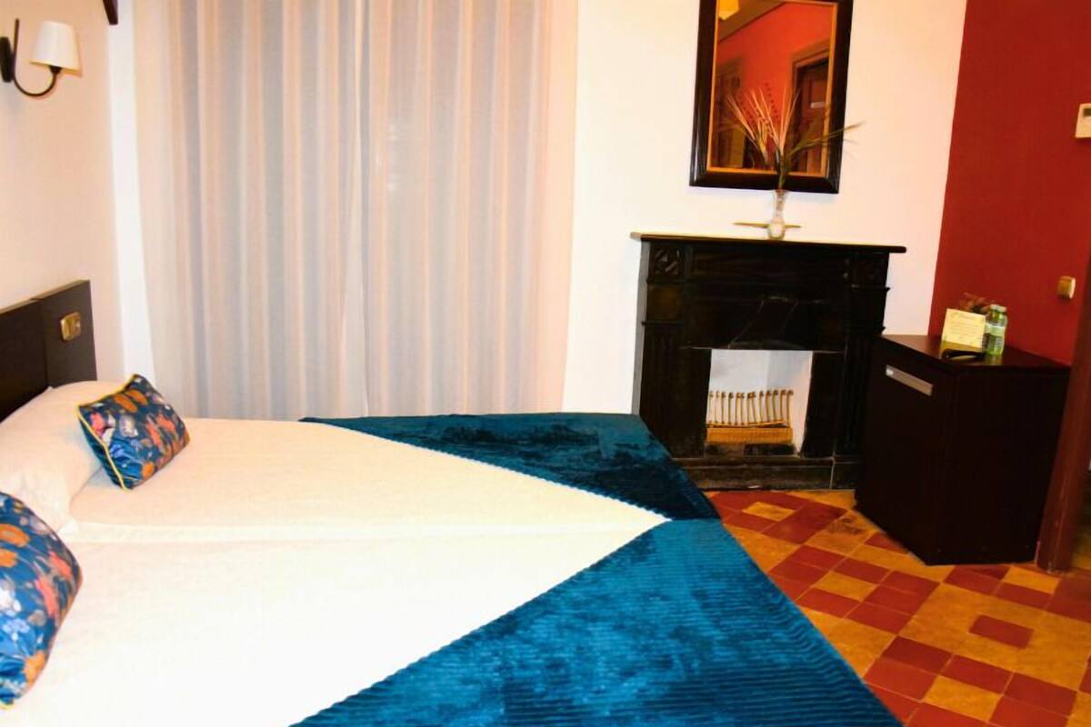 Une chambre d’hôtel avec un lit, une cheminée et un miroir au mur.