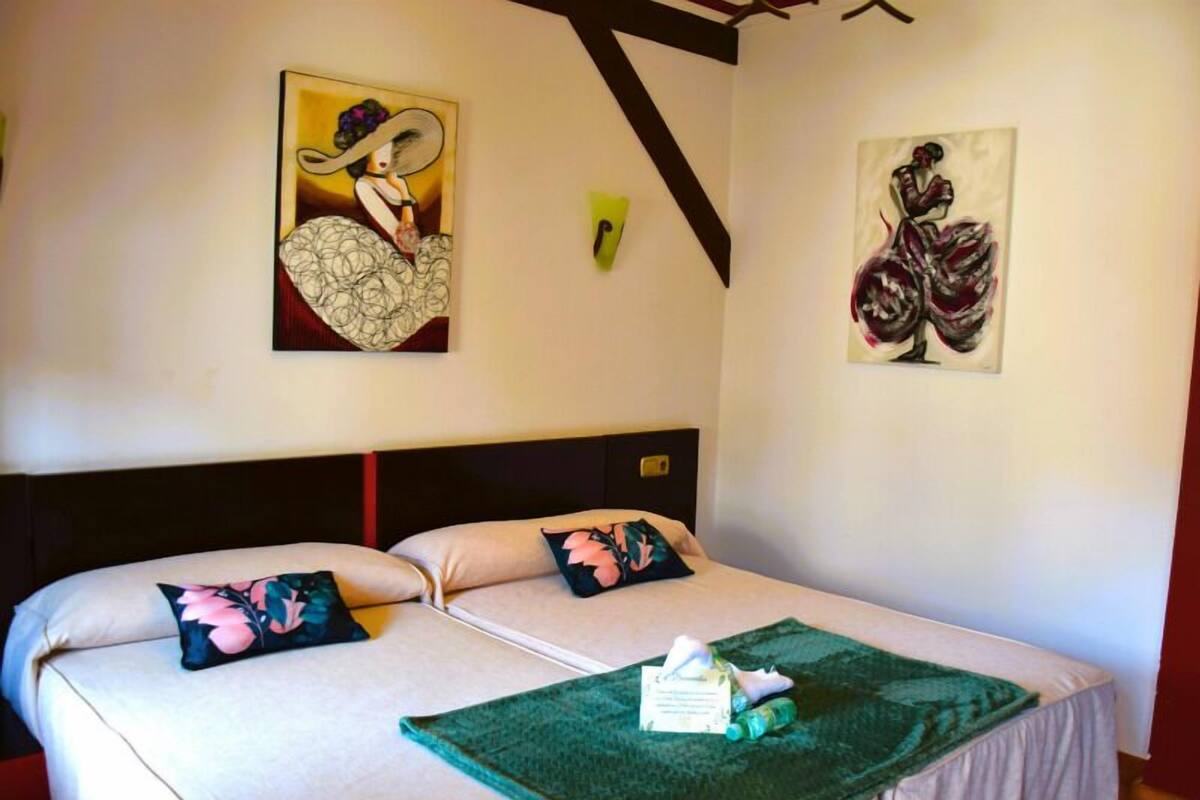 Un lit double agrémenté d’oreillers à motifs floraux, d’un plaid vert et d’œuvres d’art accrochées aux murs.
