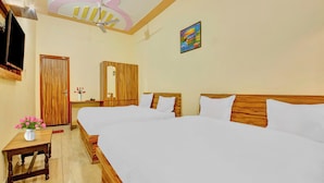 A hotel room with two beds, a wooden wardrobe, a ceiling fan, a TV mounted on the wall, and a painting.