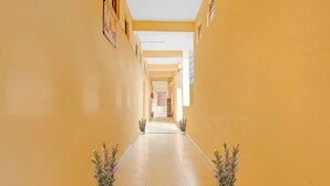 A long, narrow hallway with yellow walls and a tiled floor. There are potted plants on either side of the hallway.