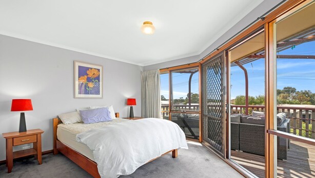A bedroom with a bed, two bedside tables, a window, and a balcony with wicker furniture. - Spacious Family Retreat on Fischer (3) (Torquay)