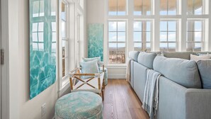 A spacious living room with a large window, a sofa, a chair, and a wall-mounted artwork.