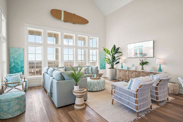 A spacious living room with a large window, a sofa, a coffee table, and a wall-mounted surfboard.