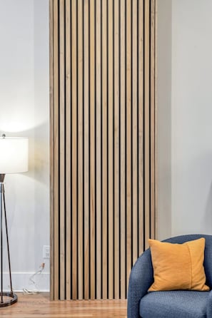 A room with a vertical wooden panel wall, a blue chair with a yellow cushion, and a floor lamp.