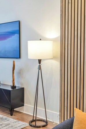 Una lámpara de pie moderna con pantalla blanca, una mesita auxiliar negra con una escultura, y un panel de pared de listones de madera.