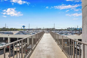 A pedestrian bridge leading to a parking area with multiple cars, a clear sky, and distant buildings. - XPLORIE ACTIVITIES & LINENS INCLUDED*! THE PLAZA - 3BR - Direct oceanfront & upgraded! (Ocean City)