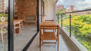 A balcony with a wooden table and chairs, a brick wall, and a view of greenery and buildings. - w Charming 3BR w Amazing Deco in Medellin (Medellín)